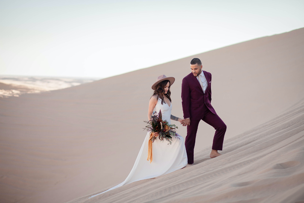 Bride and groom climbing uphill in desert