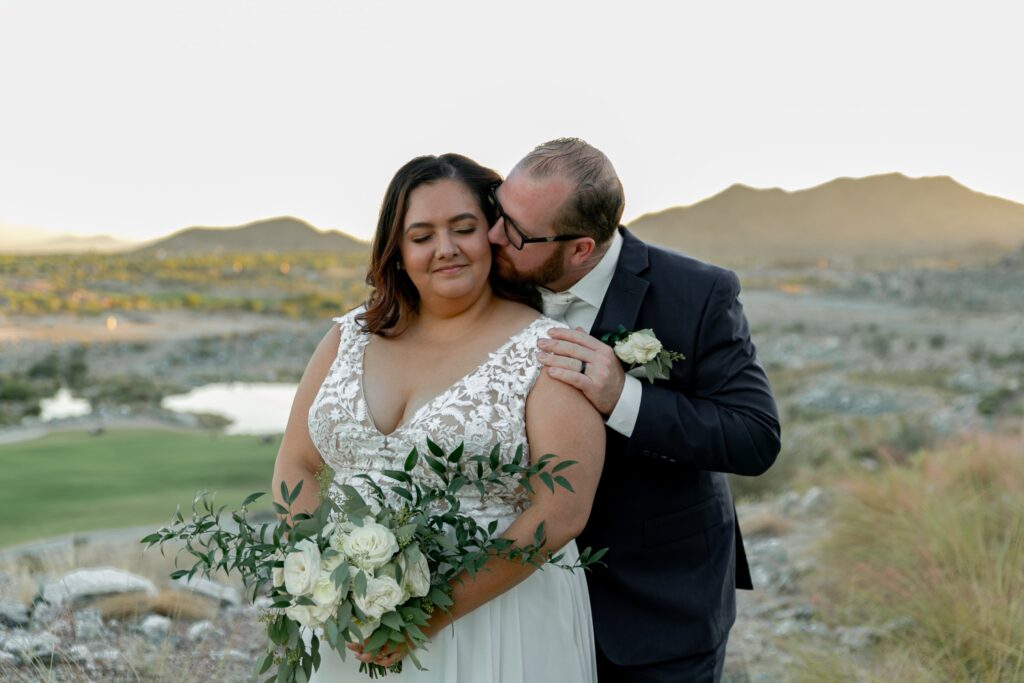 husband kissing wife on the cheek during sunset